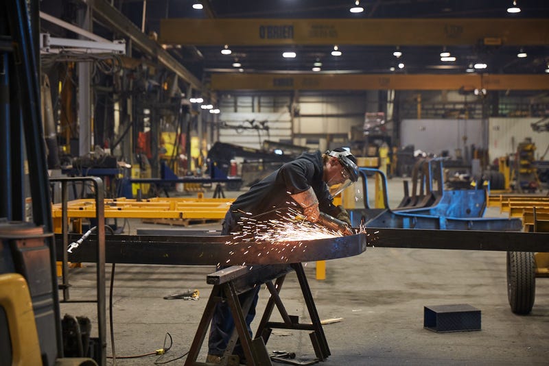 A man standing in a large workshop is using a metal grinder